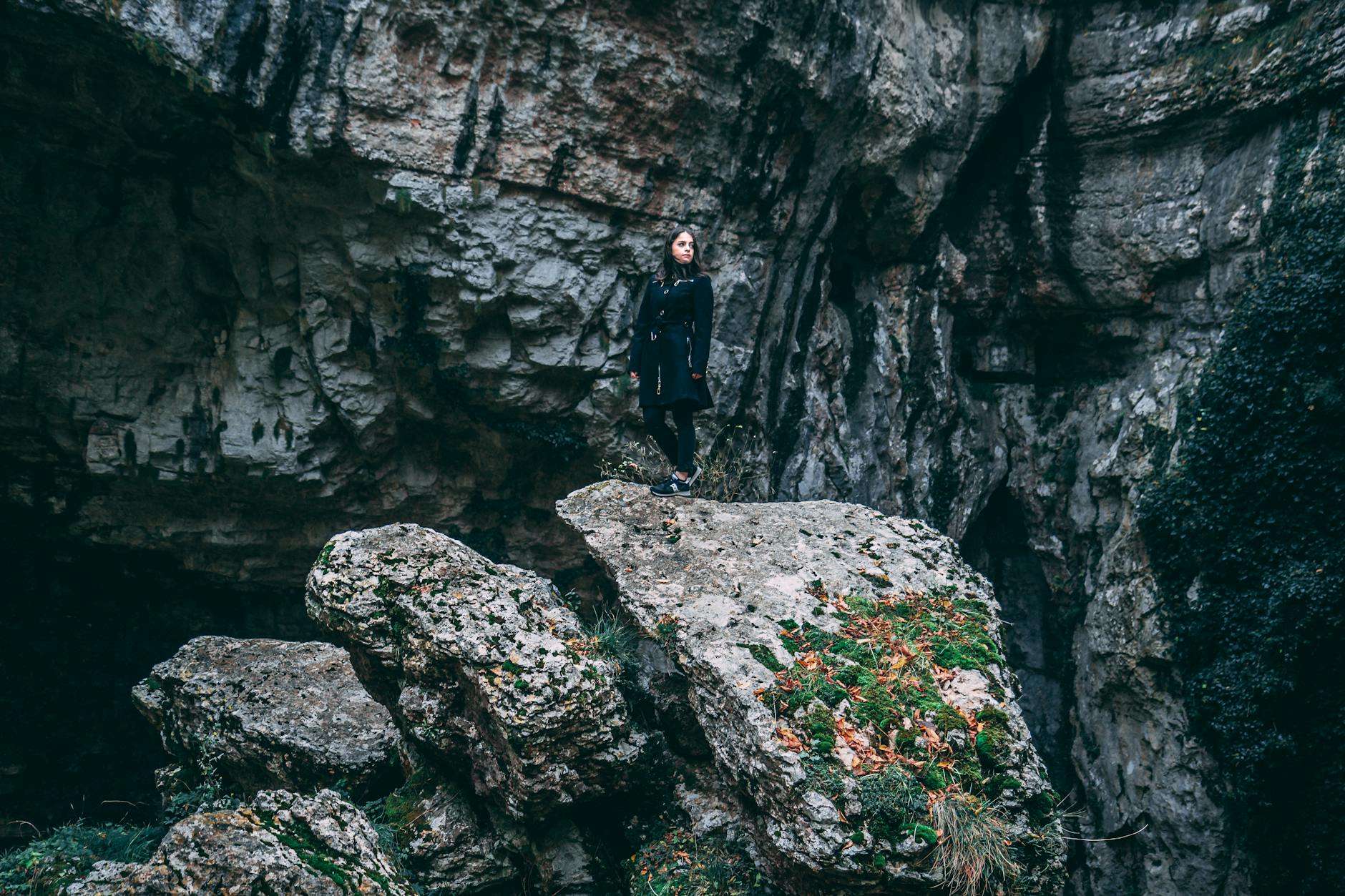 photo of woman in black outfit standing on rock